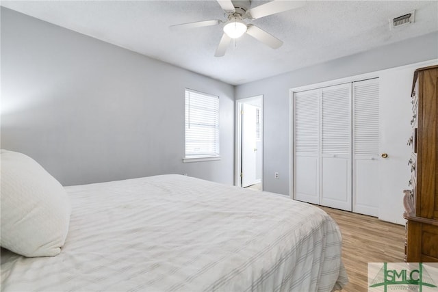 bedroom featuring ceiling fan, a textured ceiling, light wood-type flooring, and a closet