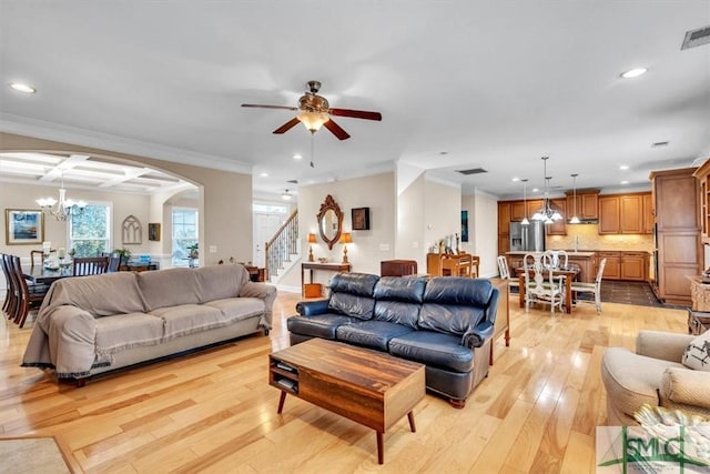 living room with ceiling fan with notable chandelier, ornamental molding, and light hardwood / wood-style floors