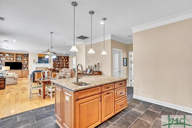 kitchen featuring decorative light fixtures, sink, ornamental molding, a kitchen island with sink, and light stone counters