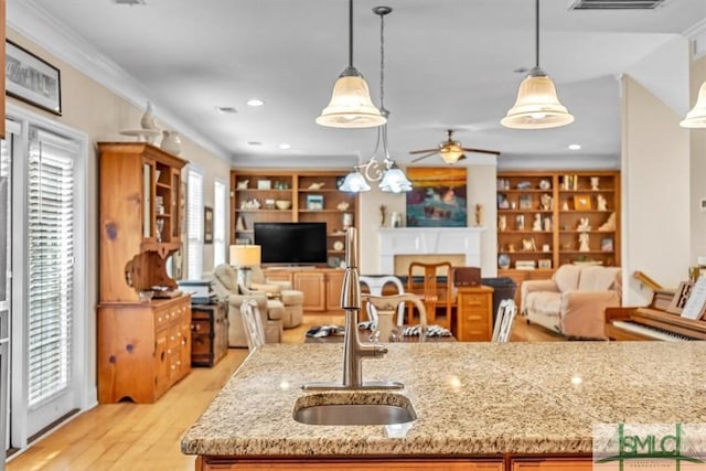 kitchen featuring sink, light stone counters, crown molding, decorative light fixtures, and light hardwood / wood-style flooring