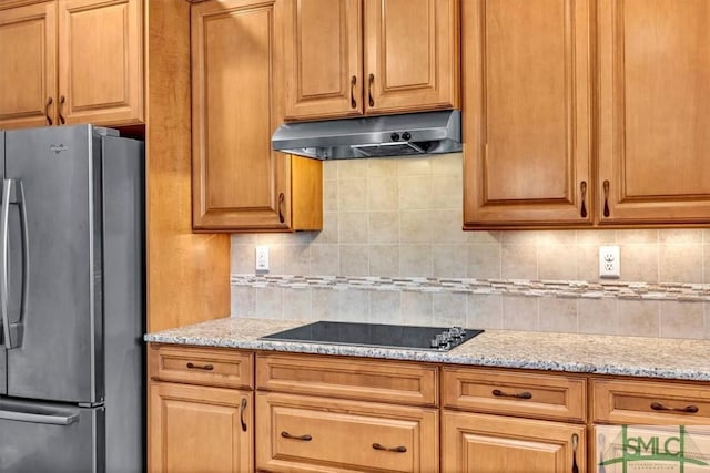 kitchen featuring black electric cooktop, stainless steel fridge, light stone counters, and decorative backsplash