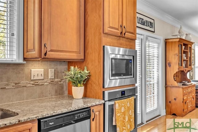 kitchen featuring decorative backsplash, ornamental molding, light stone countertops, and appliances with stainless steel finishes