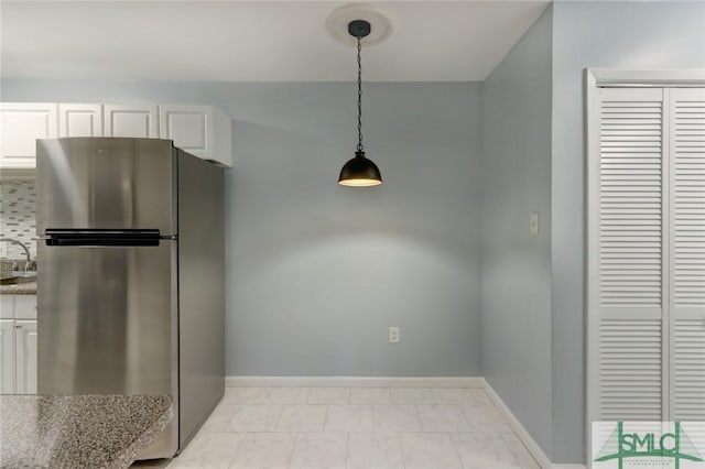 kitchen with sink, stainless steel refrigerator, hanging light fixtures, light stone countertops, and white cabinets