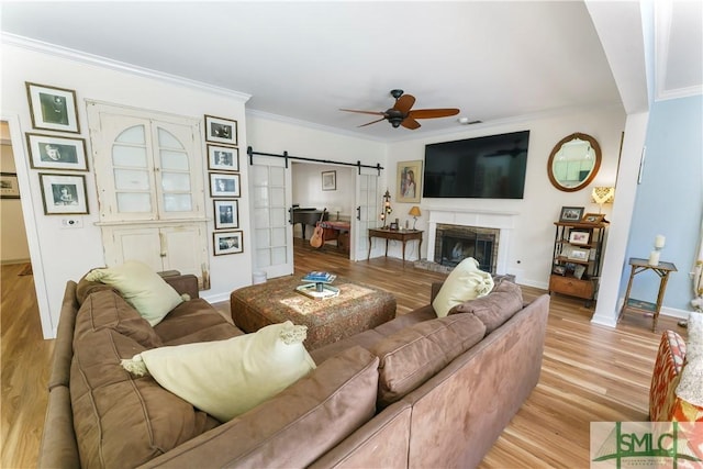 living room with crown molding, ceiling fan, a barn door, and light wood-type flooring