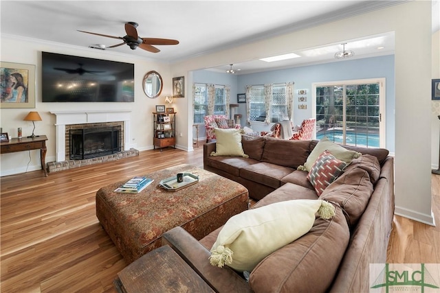 living room with crown molding, a brick fireplace, ceiling fan, and light hardwood / wood-style floors