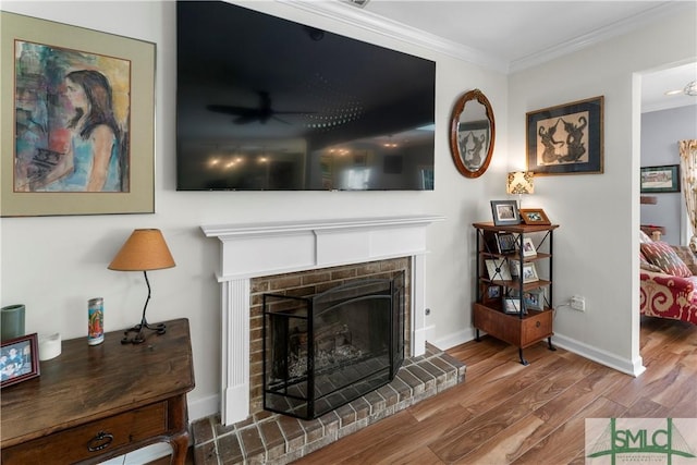 living room with ornamental molding, a brick fireplace, wood-type flooring, and ceiling fan