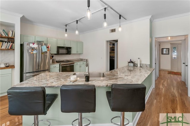 kitchen with sink, a breakfast bar, appliances with stainless steel finishes, green cabinetry, and decorative light fixtures