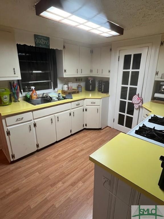 kitchen with range, sink, light hardwood / wood-style flooring, and white cabinets