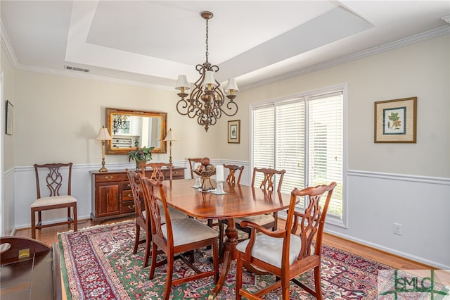 dining space with ornamental molding, a chandelier, light hardwood / wood-style floors, and a tray ceiling