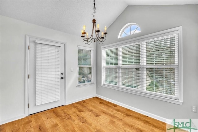 unfurnished dining area featuring hardwood / wood-style flooring, vaulted ceiling, a notable chandelier, and a textured ceiling