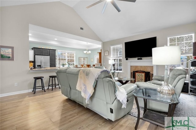 living room featuring high vaulted ceiling, ceiling fan with notable chandelier, a fireplace, and light hardwood / wood-style floors