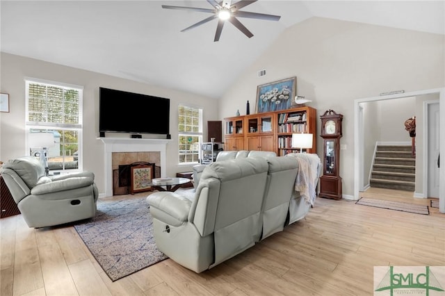 living room featuring a tiled fireplace, ceiling fan, high vaulted ceiling, and light hardwood / wood-style floors