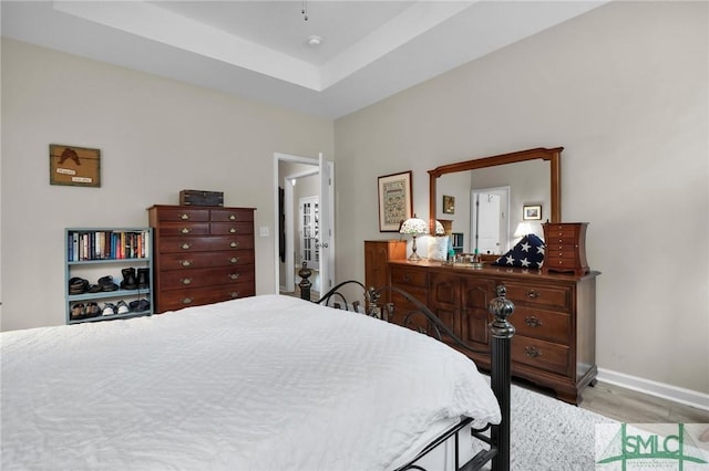 bedroom with light hardwood / wood-style flooring and a raised ceiling