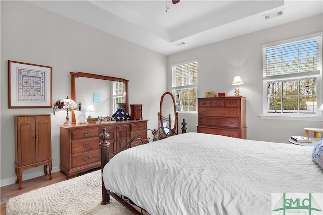 bedroom with ceiling fan, a tray ceiling, multiple windows, and light wood-type flooring