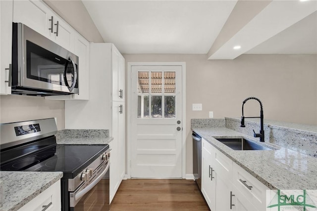 kitchen with appliances with stainless steel finishes, sink, white cabinets, dark hardwood / wood-style flooring, and light stone counters