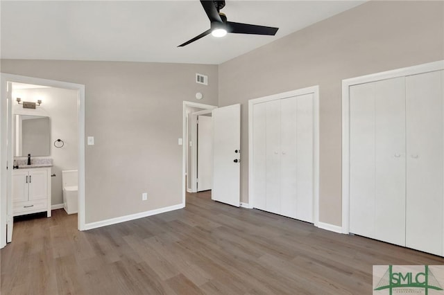 unfurnished bedroom with lofted ceiling, two closets, connected bathroom, and light wood-type flooring