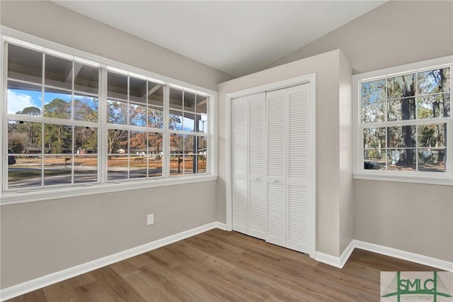 unfurnished bedroom featuring multiple windows, hardwood / wood-style floors, lofted ceiling, and a closet