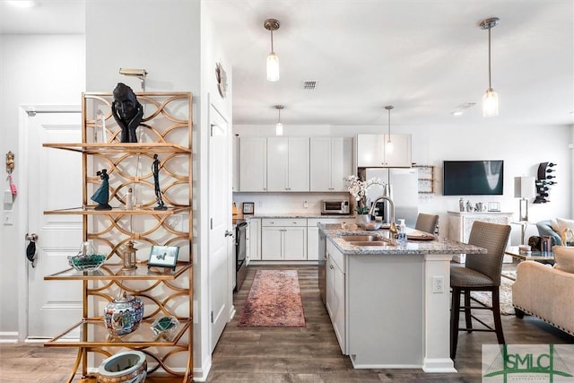 kitchen with light stone counters, decorative light fixtures, stainless steel fridge, and white cabinetry