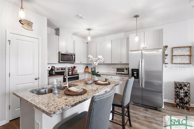 kitchen featuring a kitchen island with sink, pendant lighting, light stone countertops, and appliances with stainless steel finishes