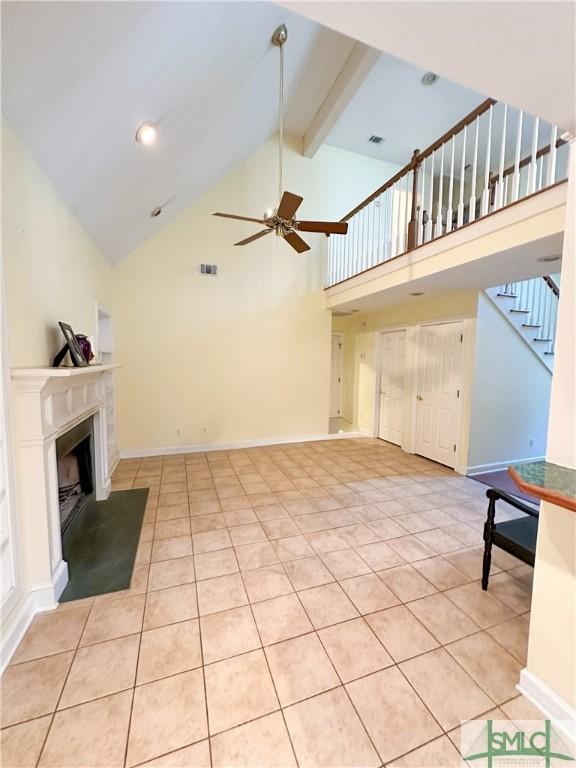 unfurnished living room featuring beam ceiling, a fireplace with raised hearth, ceiling fan, baseboards, and stairs