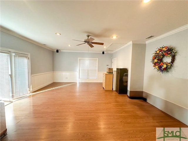 unfurnished living room featuring a wainscoted wall, ornamental molding, attic access, and light wood-style floors