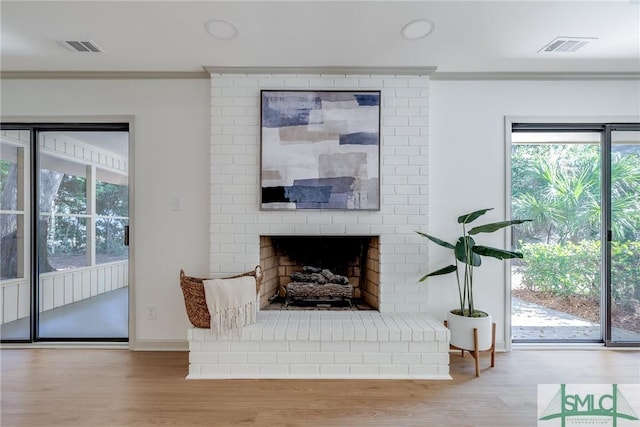 living room with ornamental molding, a brick fireplace, plenty of natural light, and light hardwood / wood-style floors