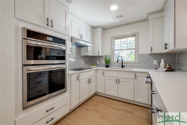 kitchen with black electric stovetop, sink, white cabinets, and stainless steel double oven