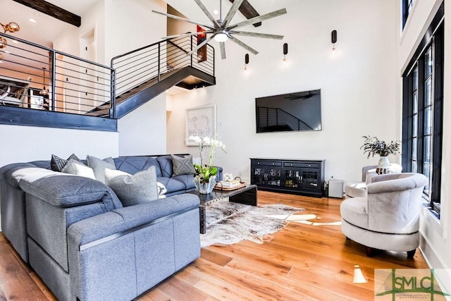 living room featuring a high ceiling, hardwood / wood-style floors, ceiling fan, and beamed ceiling