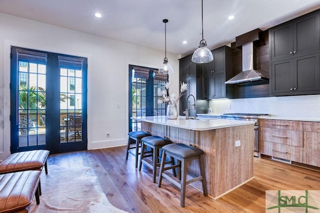 kitchen featuring wall chimney range hood, sink, a kitchen island with sink, high end stove, and decorative light fixtures