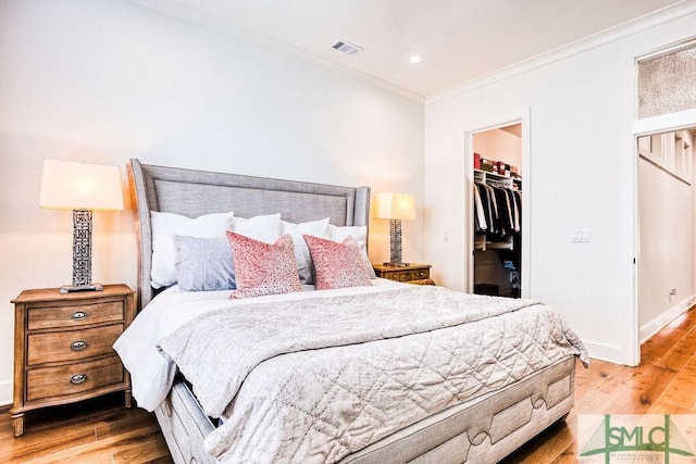 bedroom with hardwood / wood-style floors, a spacious closet, ornamental molding, and a closet