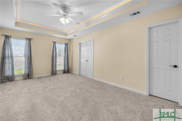 spare room with ceiling fan, light colored carpet, ornamental molding, and a raised ceiling