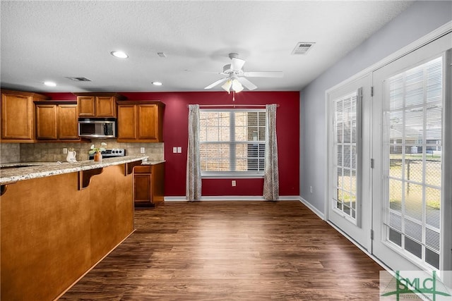 kitchen with dark hardwood / wood-style floors, a breakfast bar area, decorative backsplash, ceiling fan, and light stone countertops