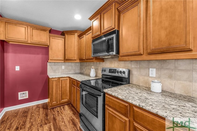 kitchen featuring hardwood / wood-style flooring, stainless steel appliances, light stone countertops, and decorative backsplash