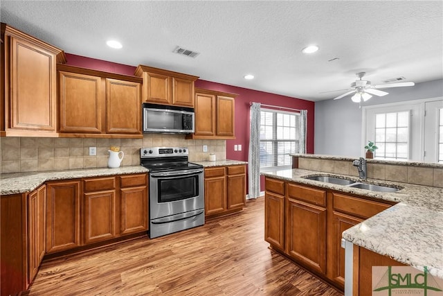 kitchen with sink, light hardwood / wood-style flooring, stainless steel appliances, tasteful backsplash, and light stone counters