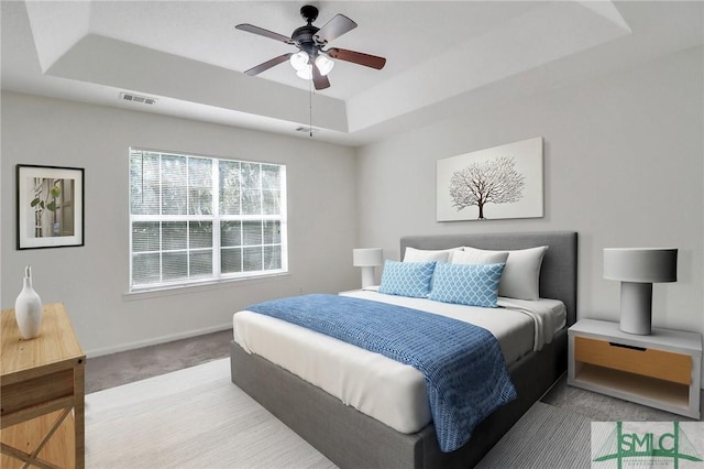 carpeted bedroom featuring ceiling fan and a tray ceiling