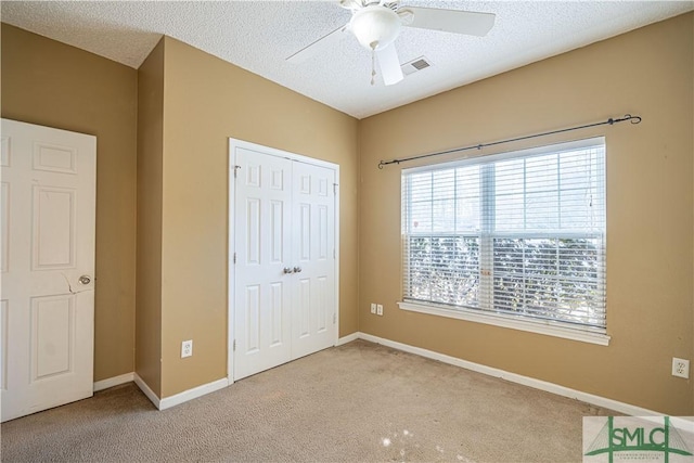 unfurnished bedroom featuring ceiling fan, a closet, light carpet, and a textured ceiling