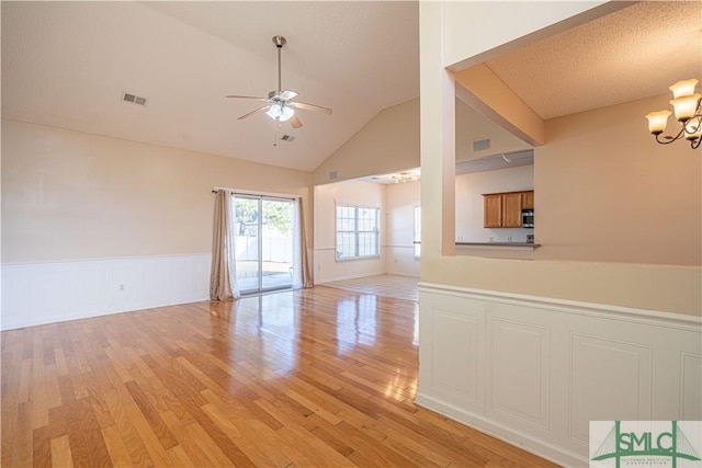 unfurnished living room with lofted ceiling, ceiling fan with notable chandelier, and light wood-type flooring