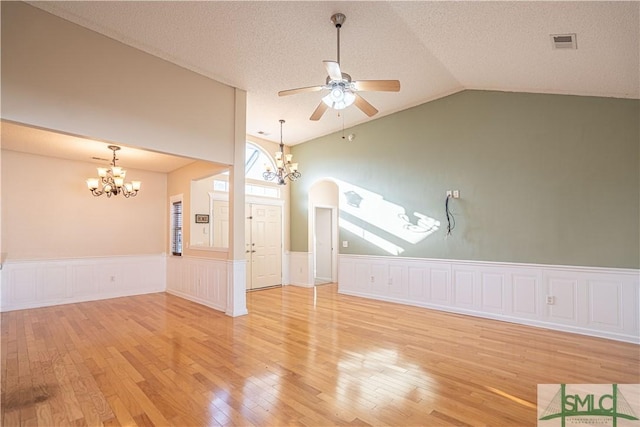 unfurnished living room with vaulted ceiling, ceiling fan with notable chandelier, a textured ceiling, and light hardwood / wood-style flooring