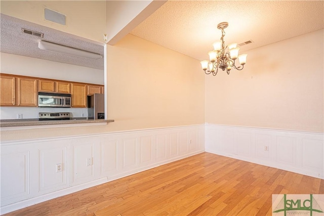 kitchen featuring hanging light fixtures, stainless steel appliances, a notable chandelier, a textured ceiling, and light wood-type flooring