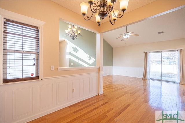 empty room with lofted ceiling, ceiling fan with notable chandelier, and light hardwood / wood-style flooring