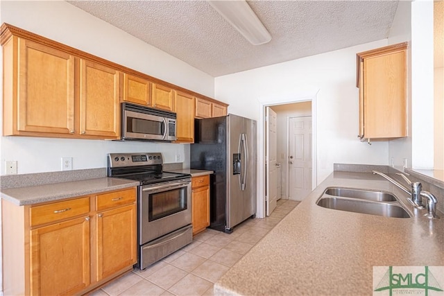 kitchen with light tile patterned flooring, appliances with stainless steel finishes, sink, and a textured ceiling