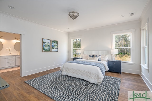 bedroom featuring wood finished floors, visible vents, baseboards, ensuite bath, and crown molding