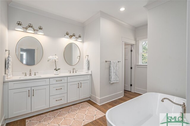 full bathroom featuring a freestanding tub, ornamental molding, a sink, and wood finished floors