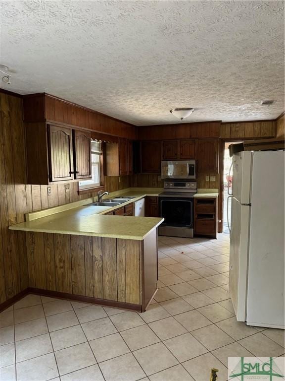 kitchen featuring stainless steel appliances, kitchen peninsula, sink, and wood walls