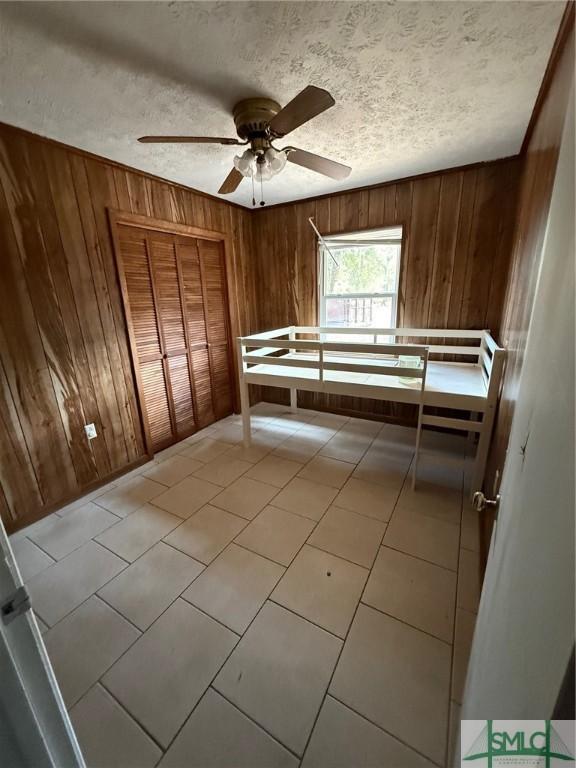 unfurnished bedroom with light tile patterned floors, a textured ceiling, and wood walls