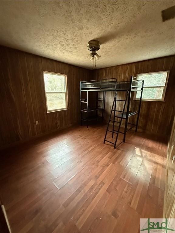 unfurnished bedroom featuring hardwood / wood-style floors, a textured ceiling, and wood walls