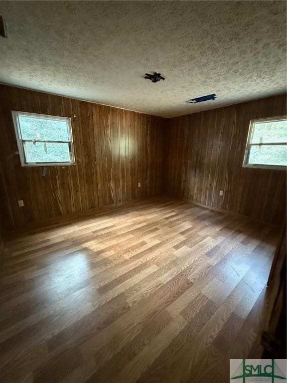 unfurnished room featuring hardwood / wood-style floors, a textured ceiling, and wood walls