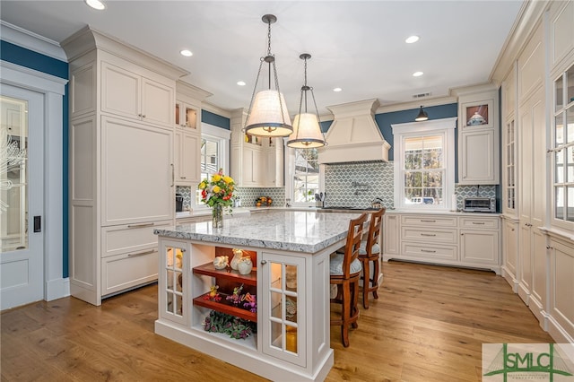 kitchen with premium range hood, light stone counters, decorative light fixtures, a kitchen island, and light hardwood / wood-style floors