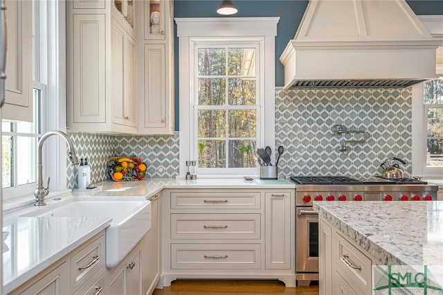 kitchen featuring sink, premium range hood, backsplash, light stone counters, and high end stove