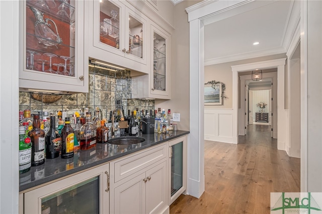 bar with sink, crown molding, light hardwood / wood-style flooring, white cabinets, and decorative backsplash